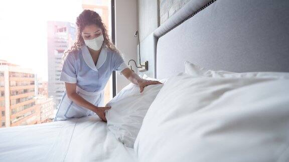 maid working at hotel bed wearing facemask